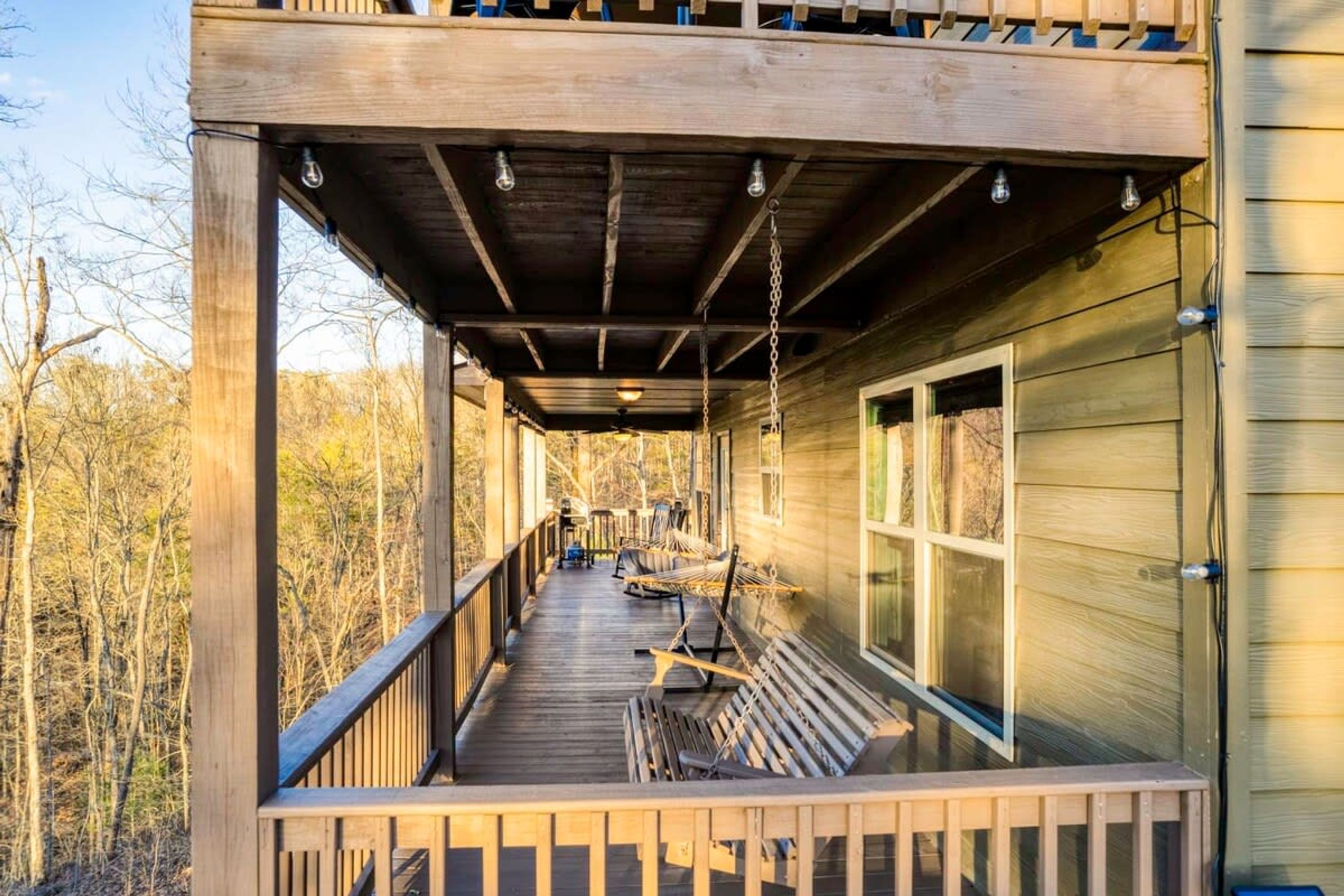 A wooden deck with a swing, a hammock, and a ceiling fan.