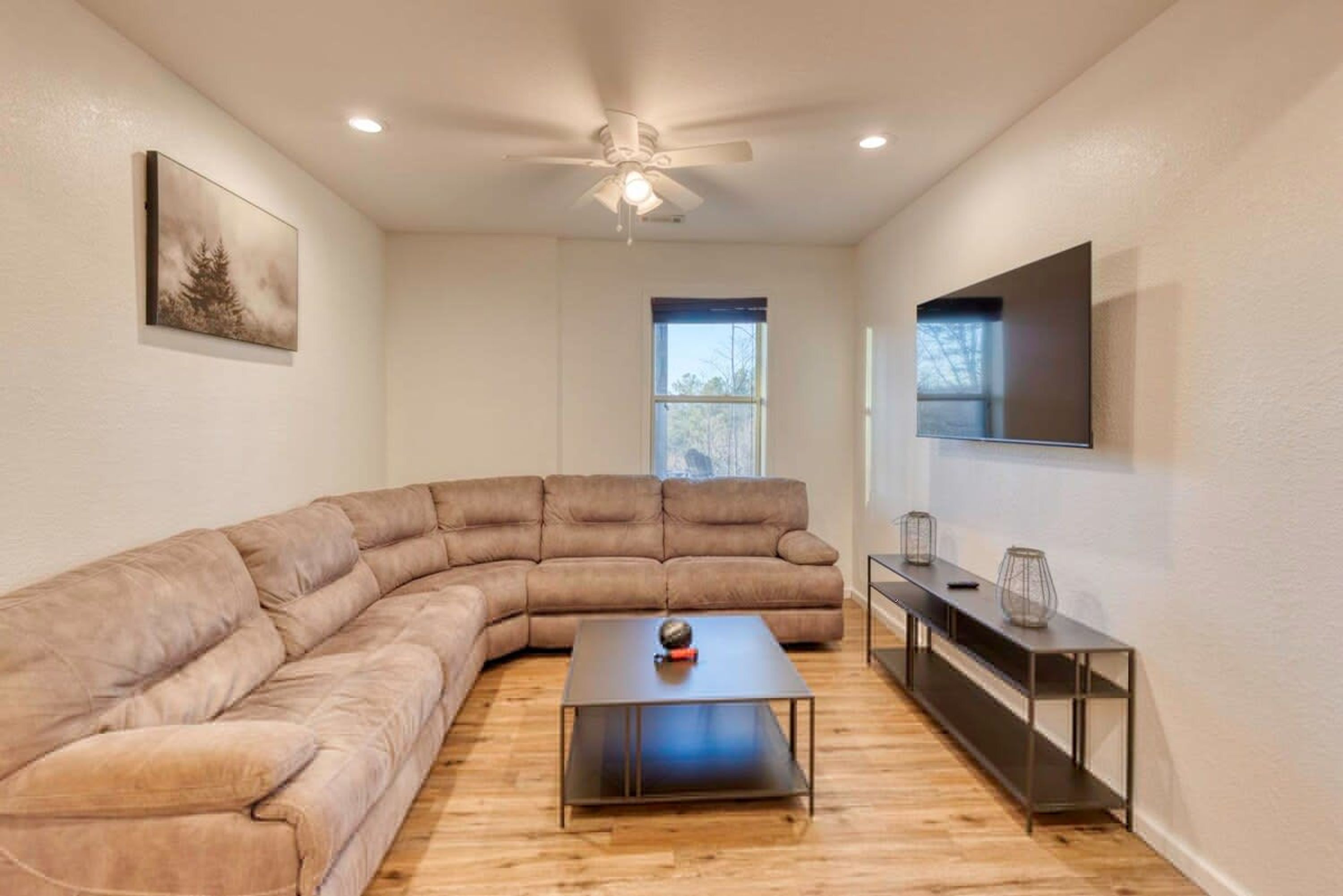 A modern living room with a sectional sofa, a coffee table, a TV, and a ceiling fan.