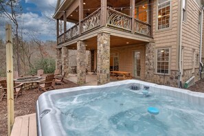 A hot tub in a backyard with stone pillars, wooden deck chairs, and a wooden deck. - Lake Lure Game Room Fire Pit Resort Access (Lake Lure)