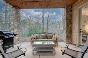 A covered patio with a stone wall, a grill, a sofa, and two chairs. - Lake Lure Game Room Fire Pit Resort Access (Lake Lure)
