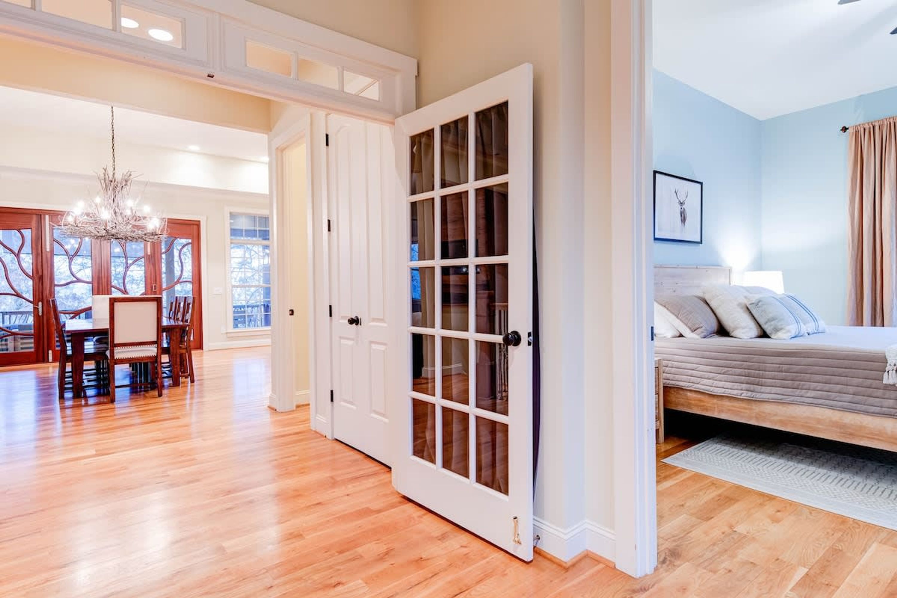 A spacious room with a large bed, a dining area with a chandelier, and a view through a glass door.