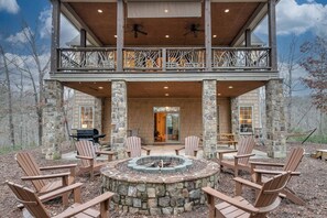 A two-story building with a stone exterior, a covered patio with Adirondack chairs, and a fire pit. - Lake Lure Game Room Fire Pit Resort Access (Lake Lure)