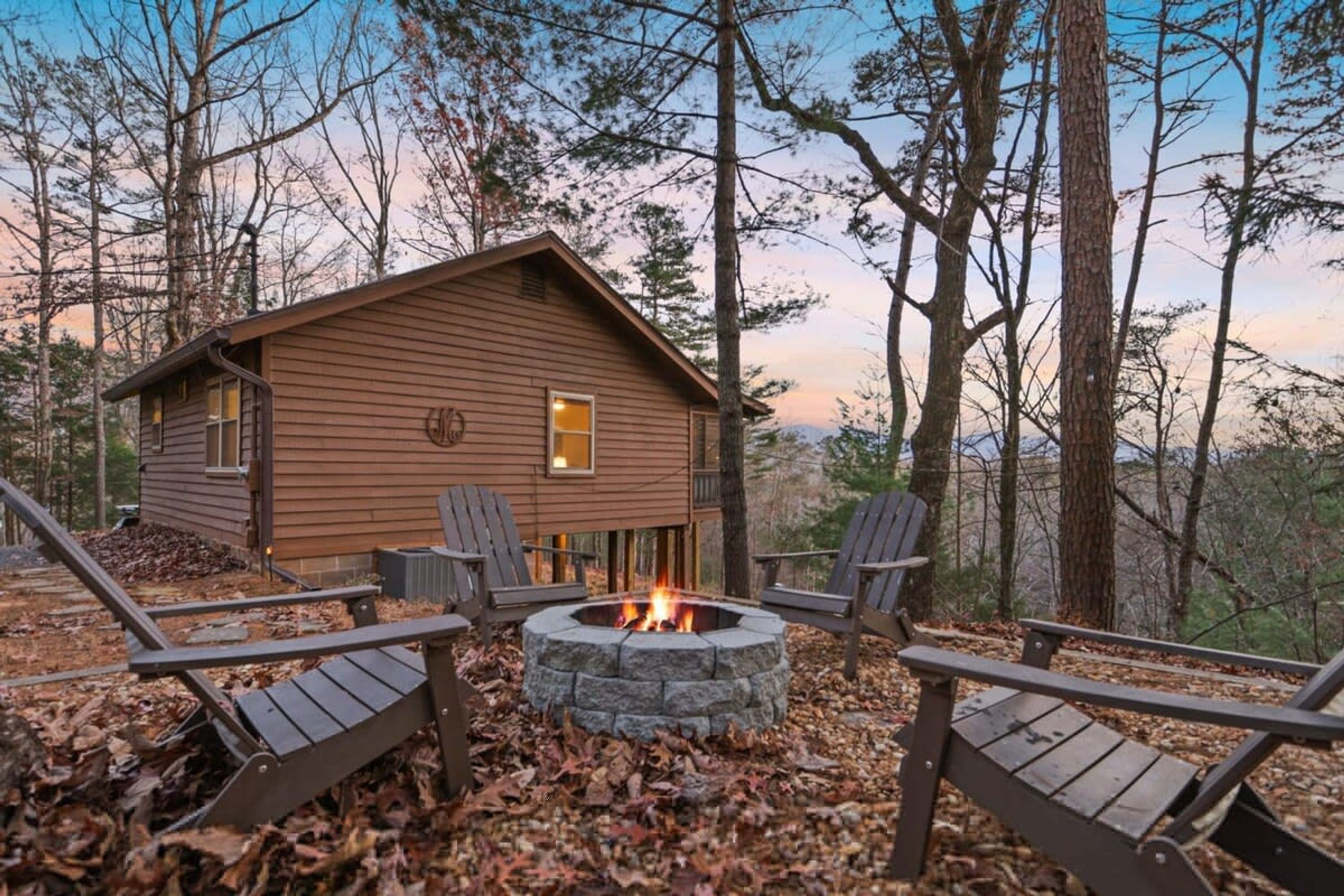 A cabin with a stone fire pit surrounded by Adirondack chairs.