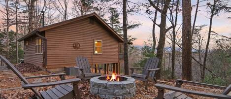 A cabin with a stone fire pit surrounded by Adirondack chairs.