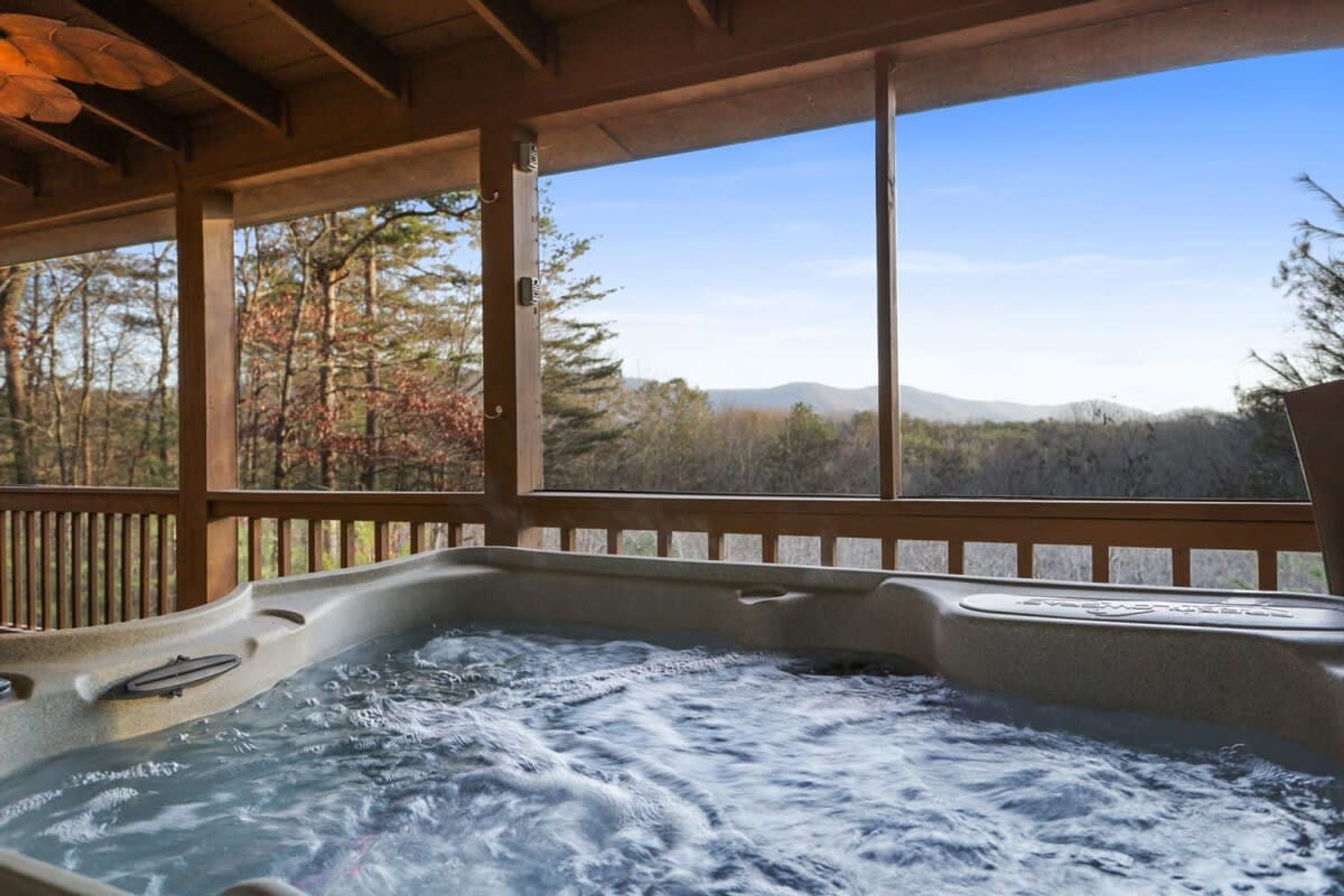 A hot tub with a wooden deck and a view of trees and mountains.