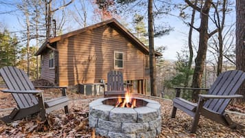 A cabin with a stone fire pit surrounded by Adirondack chairs.