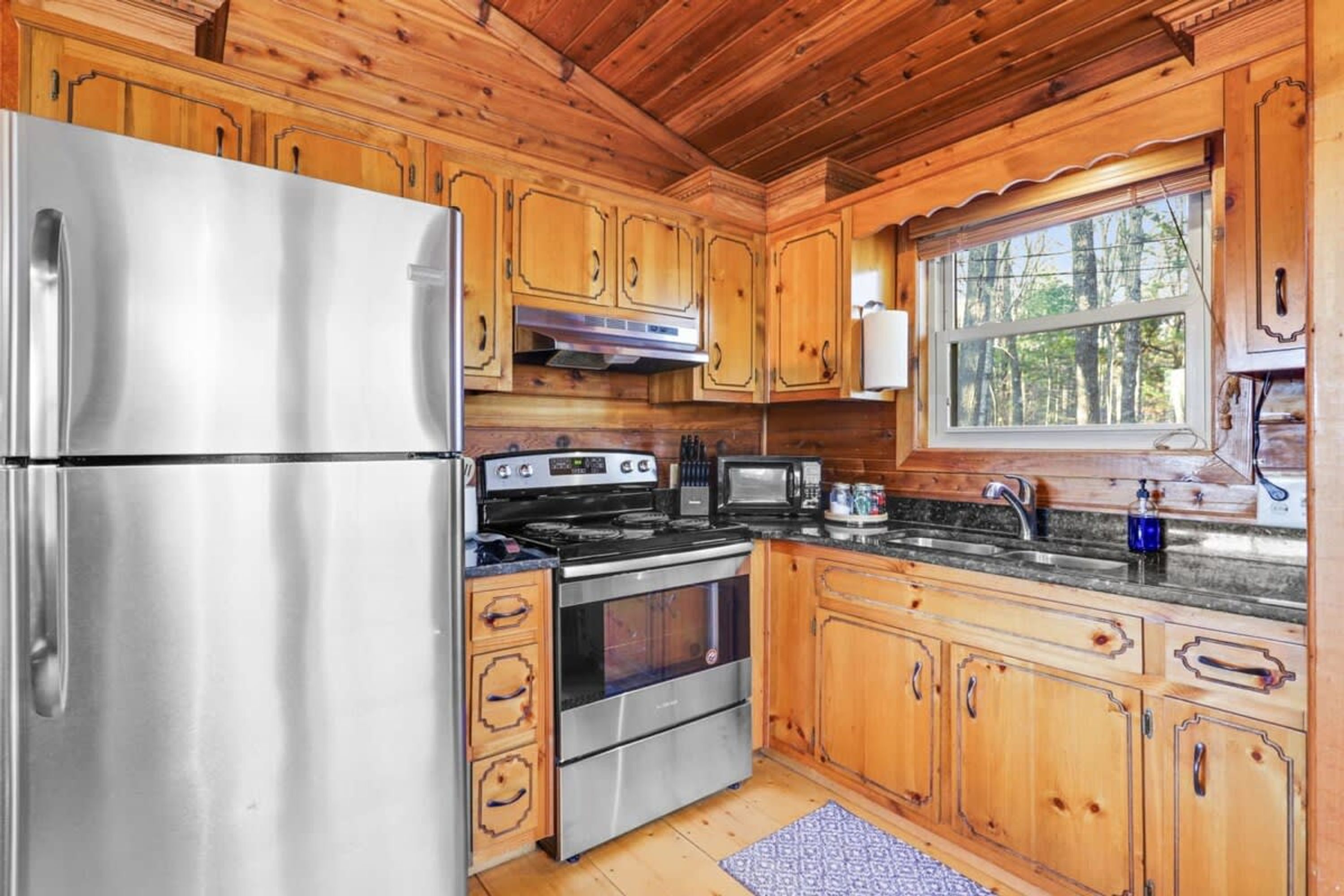 Una cocina moderna con armarios de madera, electrodomésticos de acero inoxidable y un ventanal con vista a árboles.
