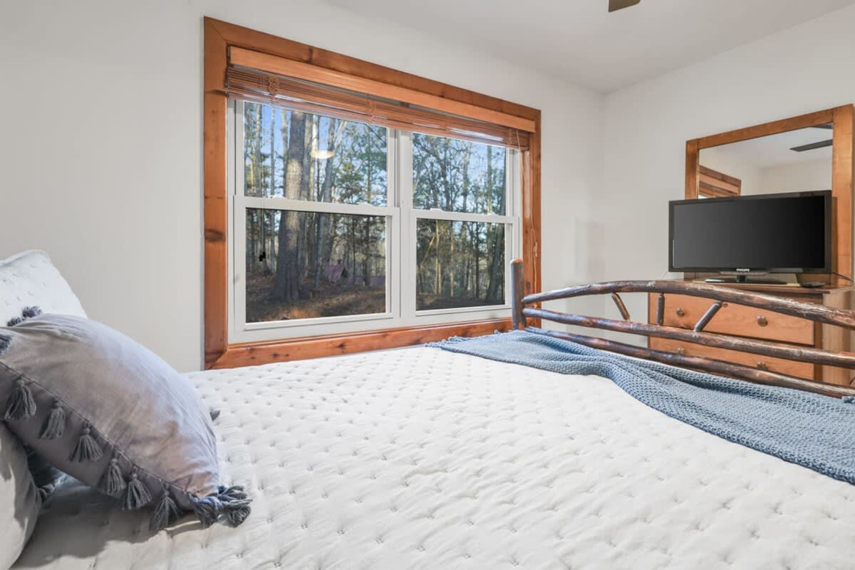 A bedroom with a large window, a bed, a television, and a dresser.