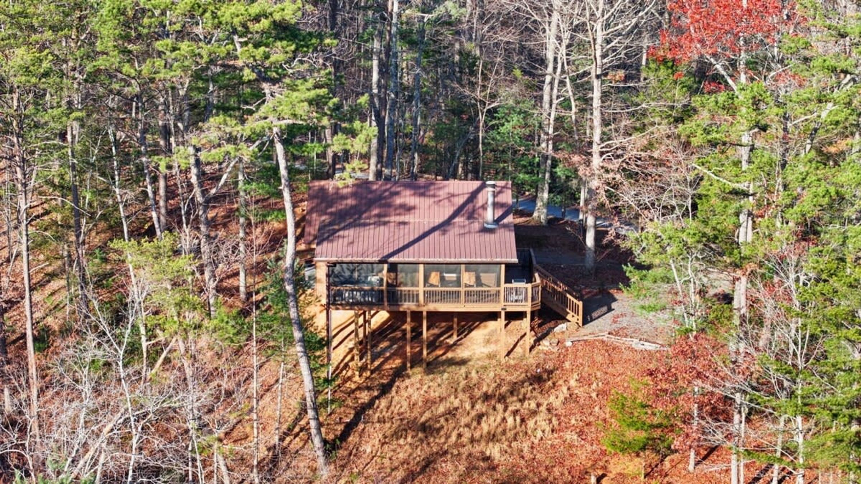 A cabin with a deck, surrounded by trees and a forested area.
