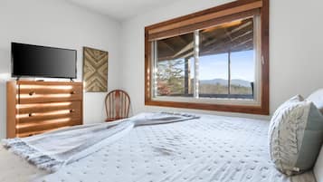 A bedroom with a bed, a dresser, a television, and a window with a view of the outdoors.