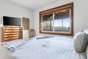 Un dormitorio con cama, cómoda, televisor y ventana con vistas al exterior.