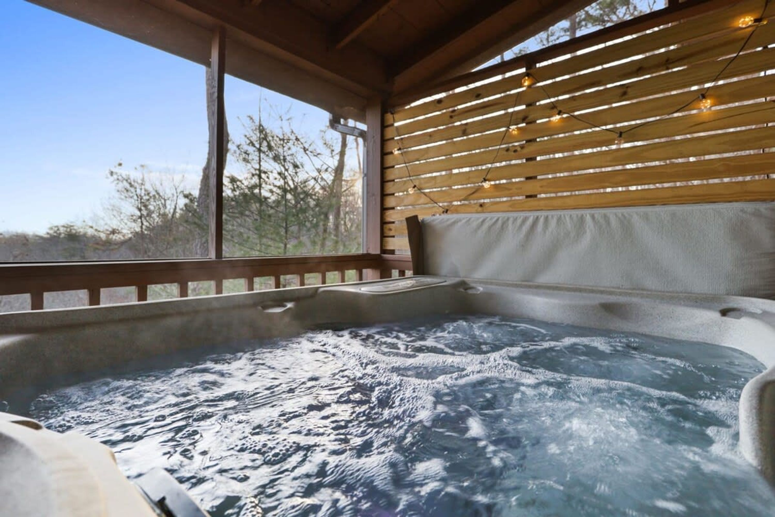 A hot tub with a wooden ceiling and a view of trees outside.