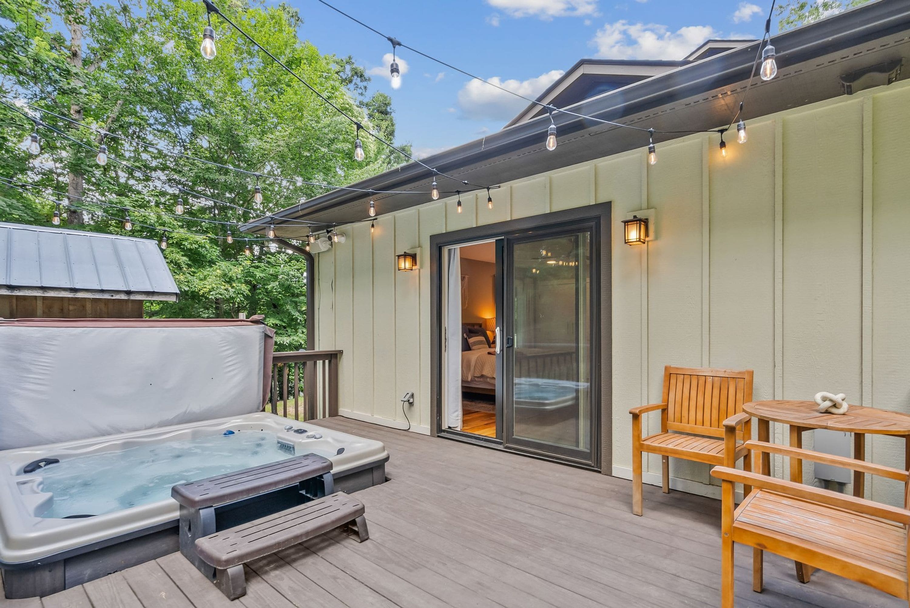 Un jacuzzi en una terraza de madera con puerta de vidrio que da a un dormitorio.
