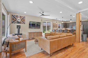 A modern living room with a sofa, a fireplace, and a dining area with chairs. - Near Asheville Hot Tub Fire Pit BBQ (Mills River)