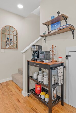 Eine Küche mit einer Kaffeemaschine, einem Bücherregal und einer Kaffeestation mit Tassen und Wasserkocher.