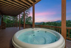 A hot tub on a wooden deck with a view of trees and hills.