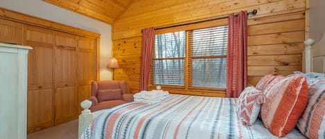 Dormitorio de cabaña de madera con una cama, una silla, un armario y una ventana con cortinas.