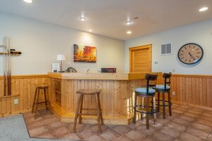 A bar area with wooden paneling, a painting, a clock, and a microwave.