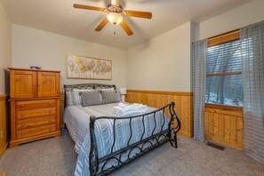 Un dormitorio con cama, cómoda de madera, ventilador de techo, obras de arte y una ventana con persianas.