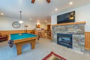 Una mesa de billar en una habitación con chimenea de piedra y un televisor montado.