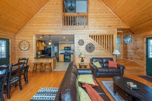 A spacious loft-style living area with a high ceiling, wooden walls, a dining table with chairs, a sofa, a coffee table, and a kitchen in the background. - 2 Deck Views Pool Table Hot Tub Spacious (Mars Hill)