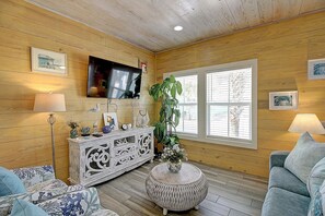A cozy living room with wooden walls, a flat-screen TV, a large window, and a comfortable seating area. - Toucan Tango- Golf Cart Friendly 3BD Home (Port Aransas)