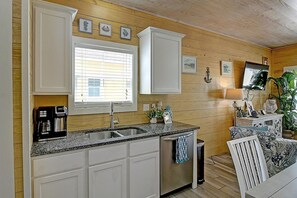 A kitchen with white cabinets, a stainless steel sink, and a window with blinds. - Toucan Tango- Golf Cart Friendly 3BD Home (Port Aransas)