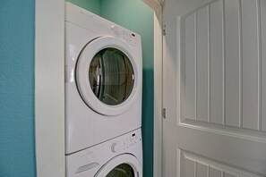Une machine à laver et un sèche-linge à chargement frontal, superposés dans une buanderie aux murs de couleur turquoise et à la porte blanche.