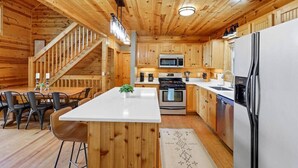 A wooden cabin interior with a kitchen, dining area, and staircase. - Views For Miles Hot Tub Pool Table Poker Table (Ellijay)