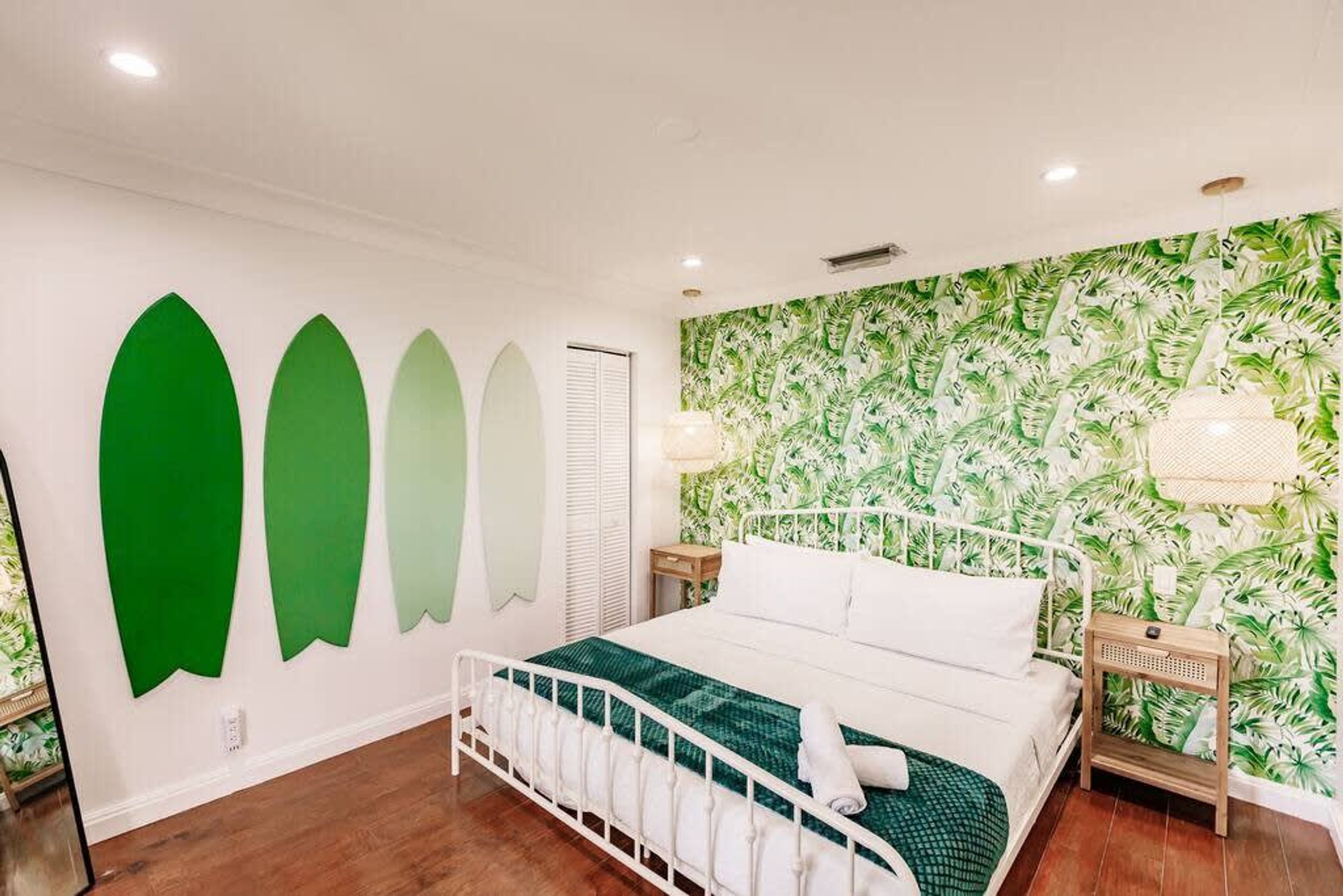 Un dormitorio con cama, mesita de noche, pared con estampado de hojas y una lámpara en el techo.