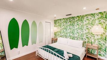 Un dormitorio con cama, mesita de noche, pared con estampado de hojas y una lámpara en el techo.