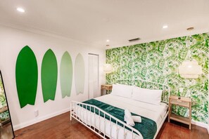 Un dormitorio con cama, mesita de noche, pared con estampado de hojas y una lámpara en el techo.