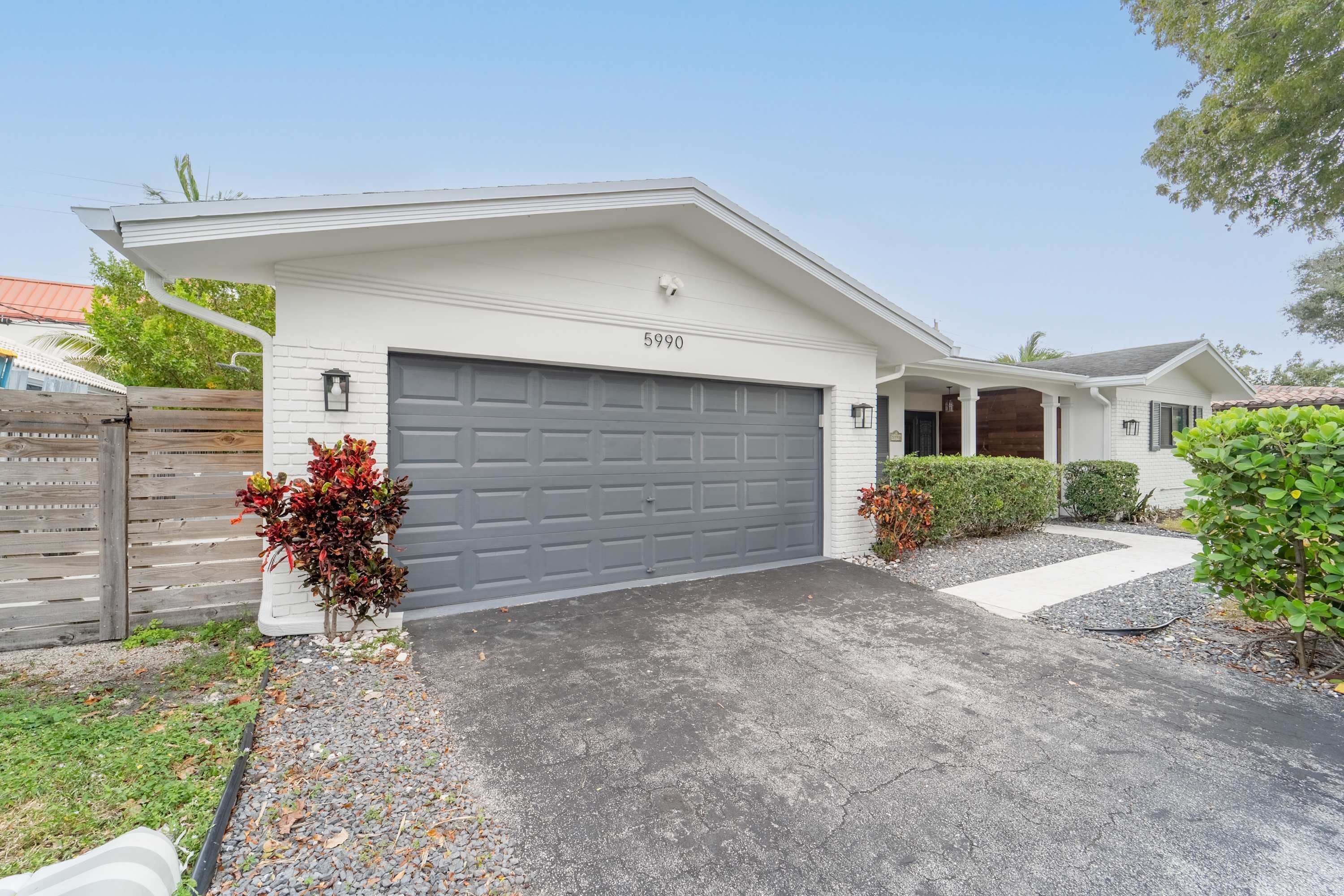 A residential house with a grey garage door, a white exterior, and a number '5990' on the wall.