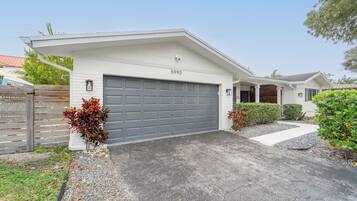 A residential house with a grey garage door, a white exterior, and a number '5990' on the wall.