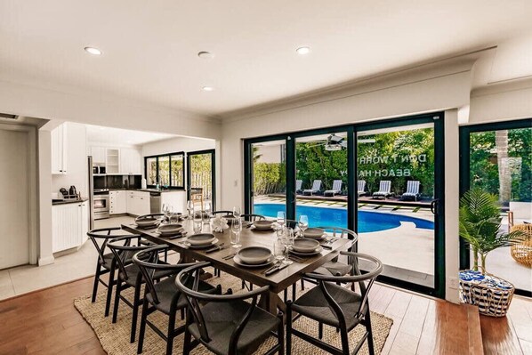A dining area with a pool view, modern kitchen, and large sliding glass doors. - Resort Style Backyard Heated Pool Hot Tub Fire Pit (Fort Lauderdale)
