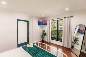 A hotel room with a bed, a window with curtains, a potted plant, and a wall-mounted TV. - Resort Style Backyard Heated Pool Hot Tub Fire Pit (Fort Lauderdale)