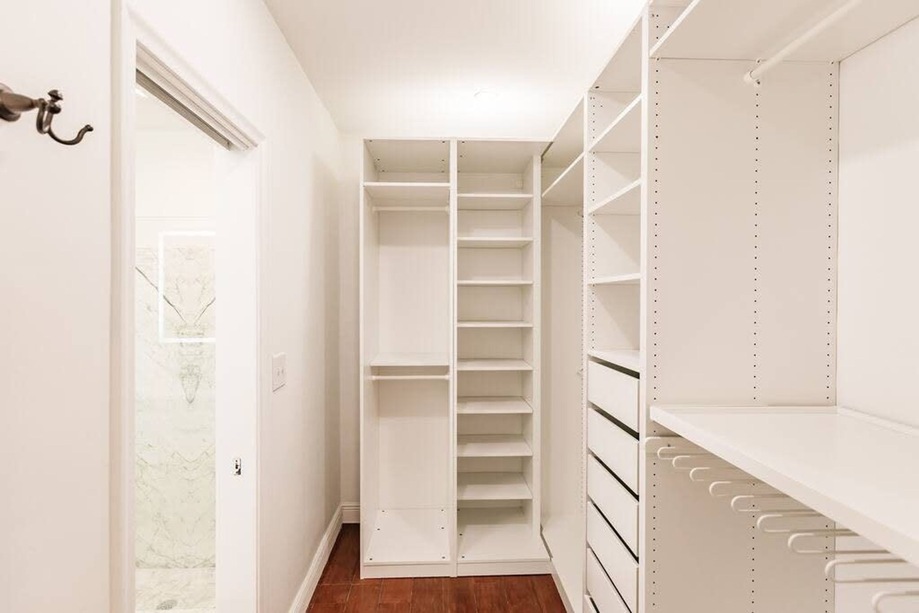 Un dressing avec de nombreuses étagères et un espace pour suspendre les vêtements, une porte dotée d’un porte-manteau et un papier peint à motifs sur le mur adjacent.
