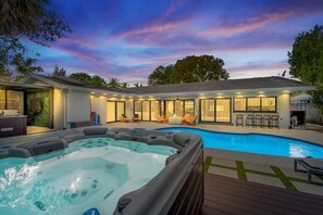 Un espace piscine extérieur moderne, doté d’un jacuzzi, de chaises longues et d’un patio couvert.