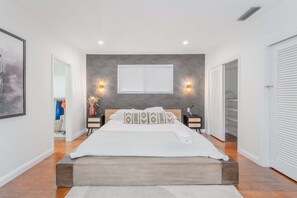 A modern bedroom with a large bed, bedside lamps, a window with blinds, and a wardrobe. - Resort Style Backyard Heated Pool Hot Tub Fire Pit (Fort Lauderdale)