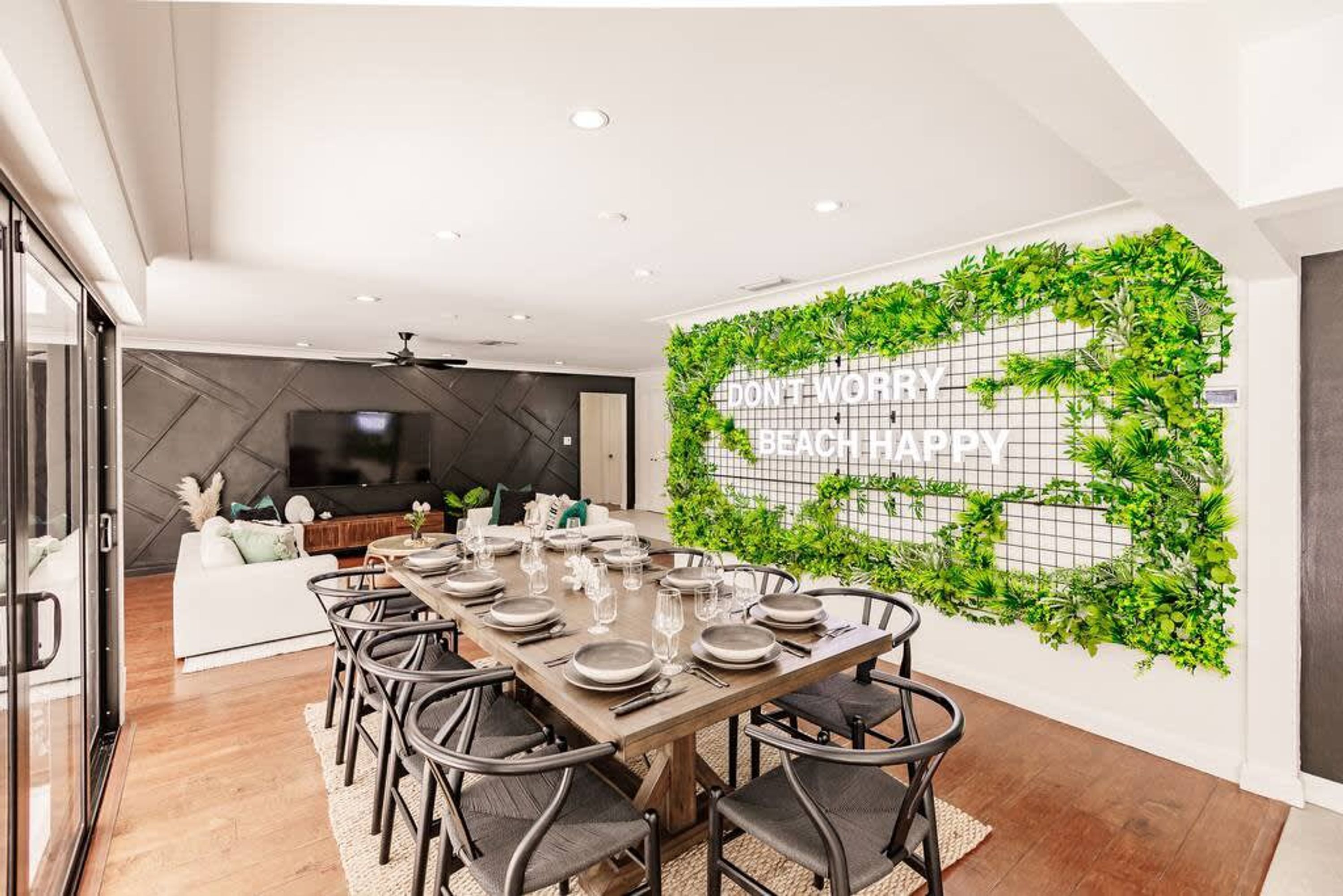 A dining area with a long table set for six, surrounded by chairs, with a modern kitchen in the background.