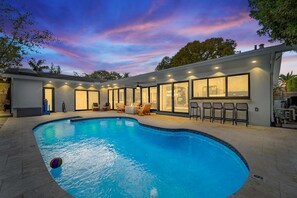 Une maison moderne dotée d’une piscine, de grandes fenêtres et d’un espace salon extérieur.