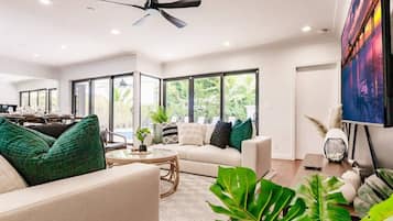 Un salon spacieux doté d’un ventilateur de plafond, de grandes fenêtres, d’un canapé, d’une table basse et d’un tableau accroché au mur.