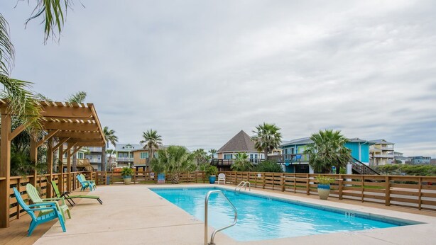 Ein Schwimmbecken mit Holzterrasse, Liegestühlen und einer überdachten Pergola.