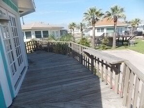 A wooden deck with a railing, leading to a building with a white facade and a window with a grid pattern. - Beach Shak- Pool View Private Apartment (Port Aransas)