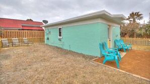A small, single-story building with a light blue exterior, a red roof, and a fenced backyard. There are four turquoise chairs outside. - Kona Cottage Dog Friendly In Town Location (Port Aransas)