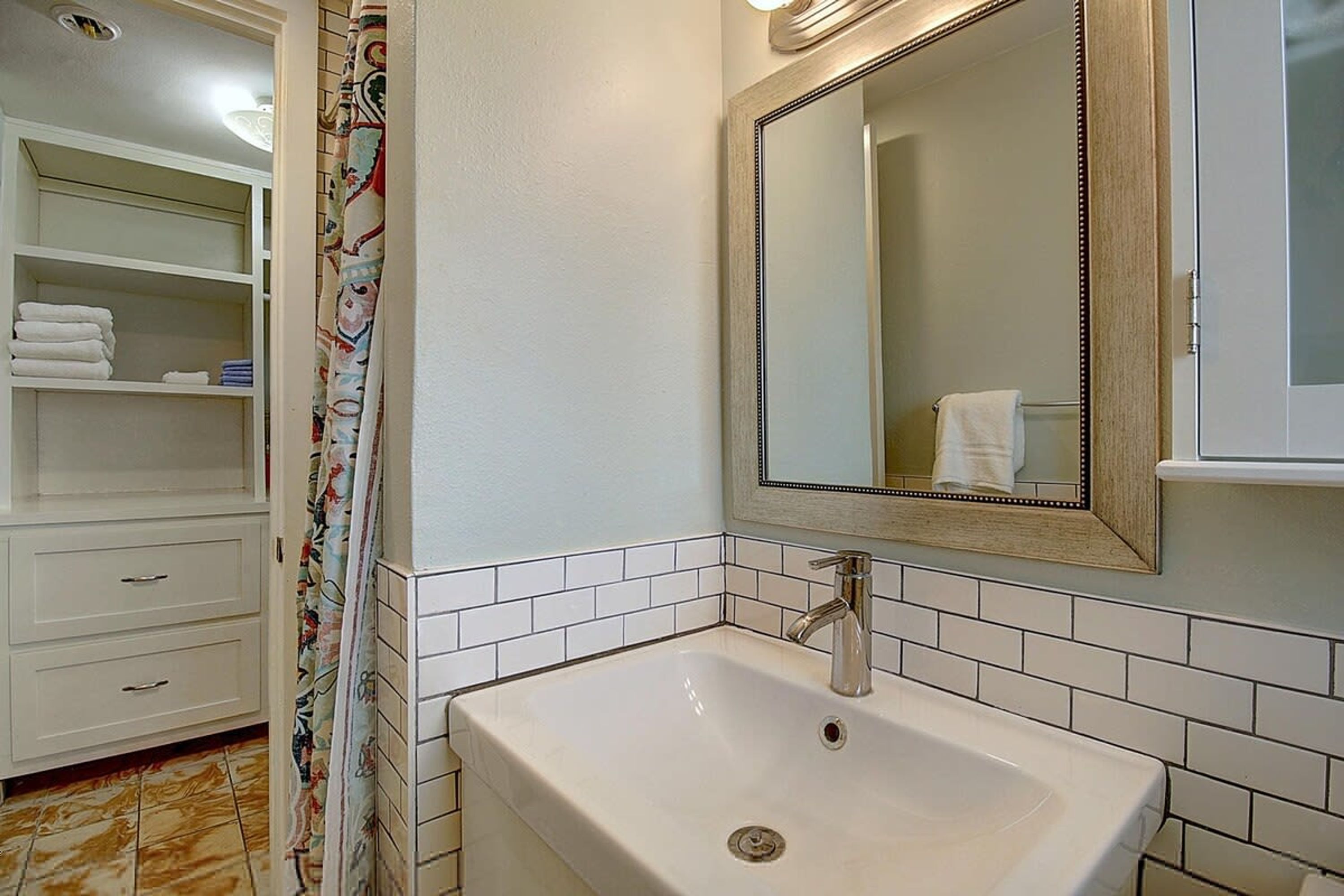 A bathroom with a white sink, a mirror, and a tiled wall.