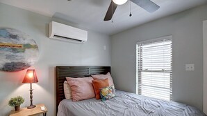A bedroom with a bed, a nightstand, a lamp, a ceiling fan, and a window with blinds. - Kona Cottage Dog Friendly In Town Location (Port Aransas)