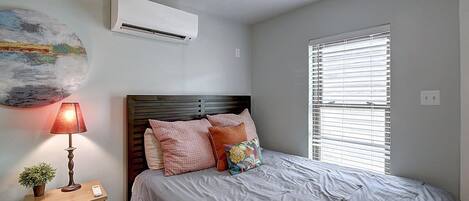 Un dormitorio con cama, mesita de noche, lámpara, ventilador de techo y ventana con persianas.