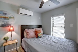 Ein Schlafzimmer mit einem Bett, einem Nachttisch, einer Lampe, einem Deckenventilator und einem Fenster mit Jalousien.