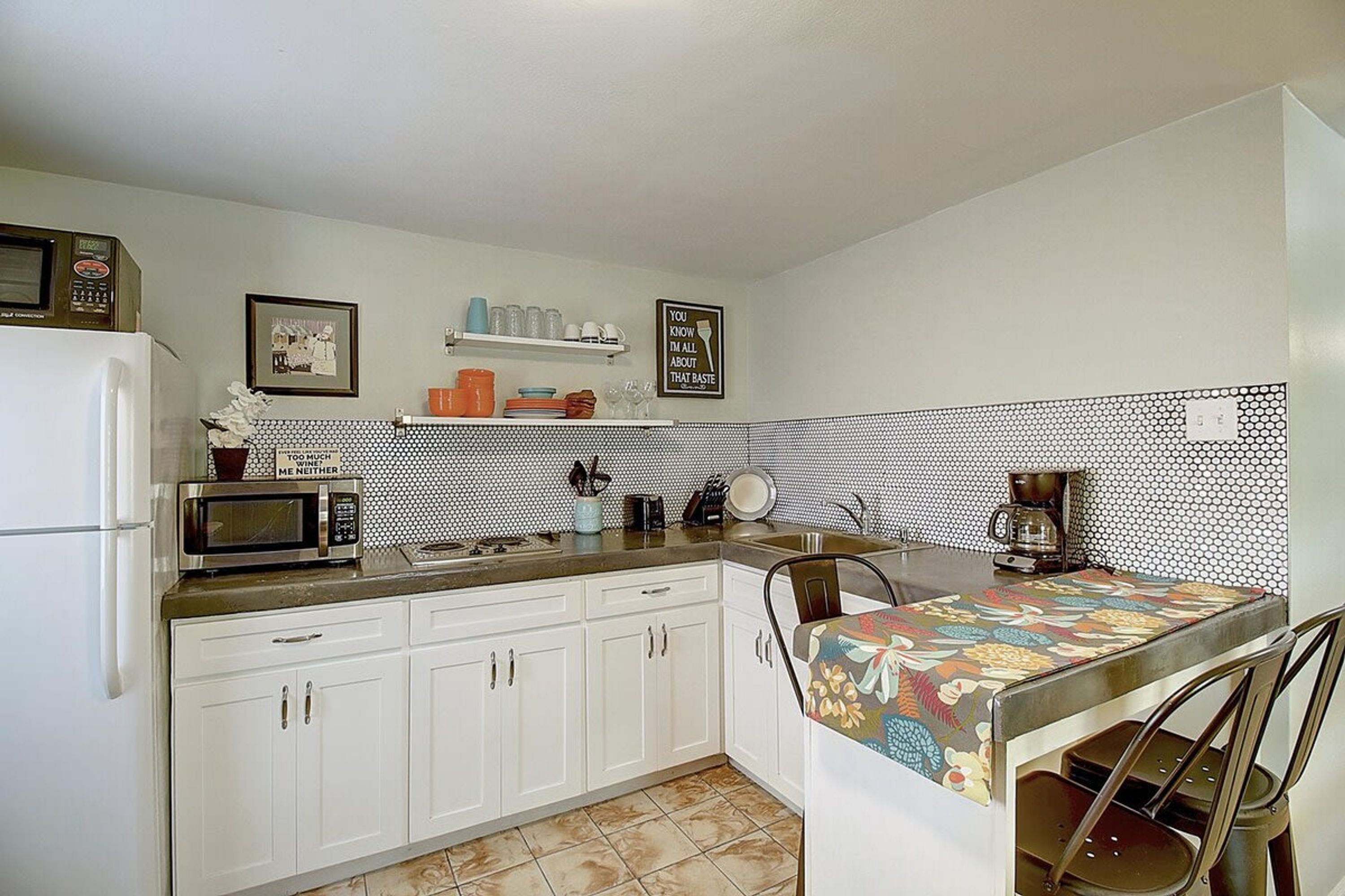 Cocina compacta con armarios blancos, microondas, cafetera y salpicadero de azulejos.